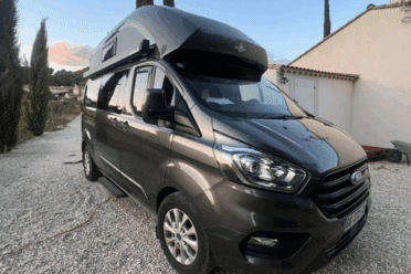 Fourgon aménagé gris stationné en extérieur au crépuscule